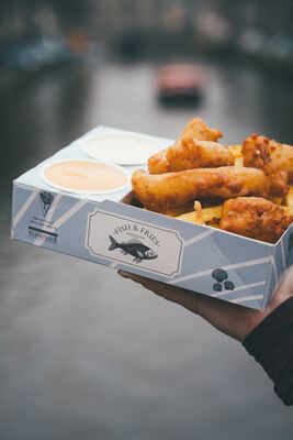 Fish & Fries box held over the Singel canal with Amsterdam canal houses