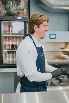 Chef smiling in profile, wearing the Fish & Fries apron with drinks fridge behind
