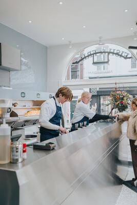 Inside Fish & Fries: clean stainless steel counter with both staff and a customer
