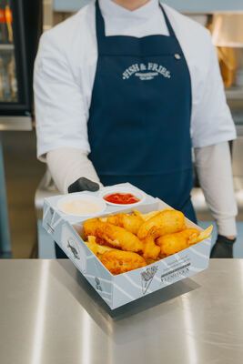 Staff presenting a box of fish and fries on the counter, apron logo visible